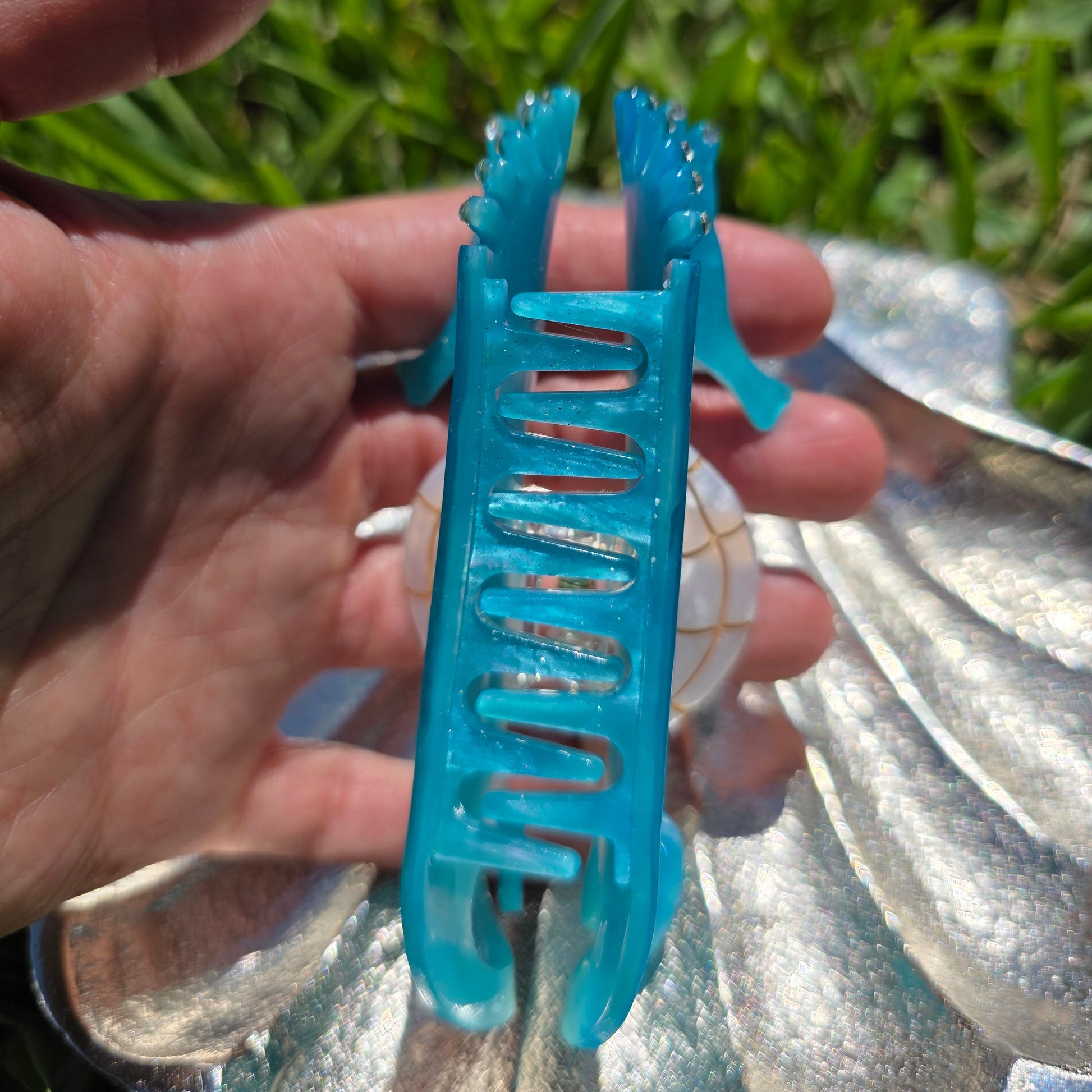 Blue hair clip held in a hand view of side 